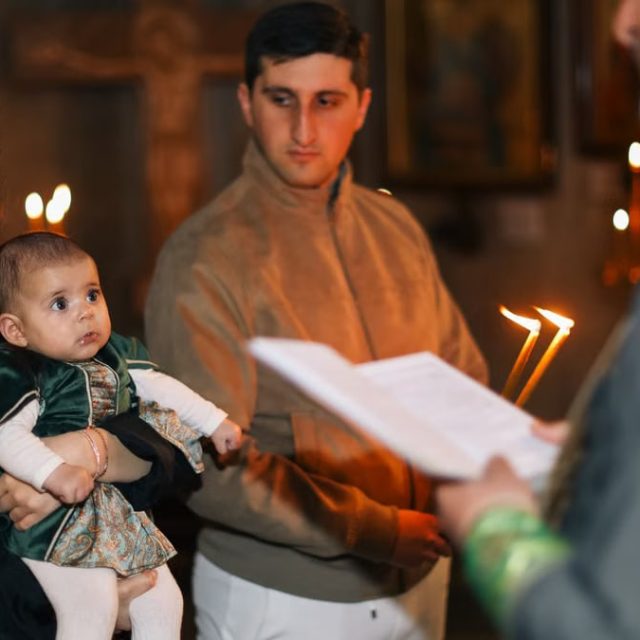 A family participates in a traditional religious ceremony with candlelight indoors.